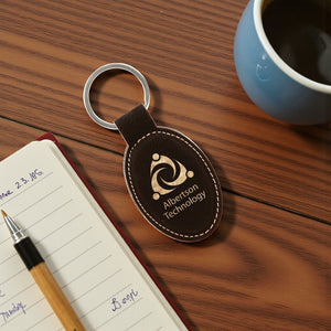black leatherette keychain with logo on a wooden desk with a notebook and pen.
