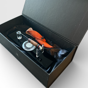 Open black box containing a bow tie and other accessories on a light gray background