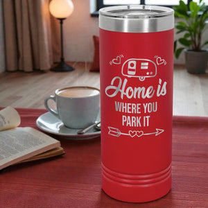Red thermos with 'Home is where you park it' text on a table with a cup of coffee and book.