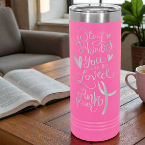 Pink tumbler with motivational quote on a wooden table with a book and cup in the background.