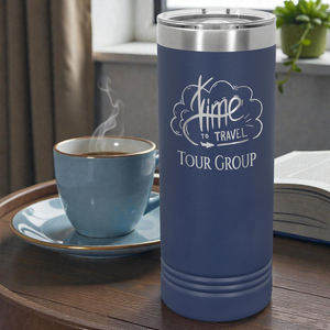 Navy Blue insulated tumbler with 'Time to Travel Tour Group' logo next to a steaming cup of coffee on a wooden table.