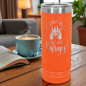 Orange tumbler with 'Camping is my therapy' text on a wooden table with a cup and book.