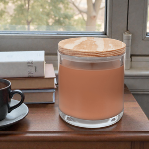 Glass jar with wooden lid on a table next to a cup of coffee and books
